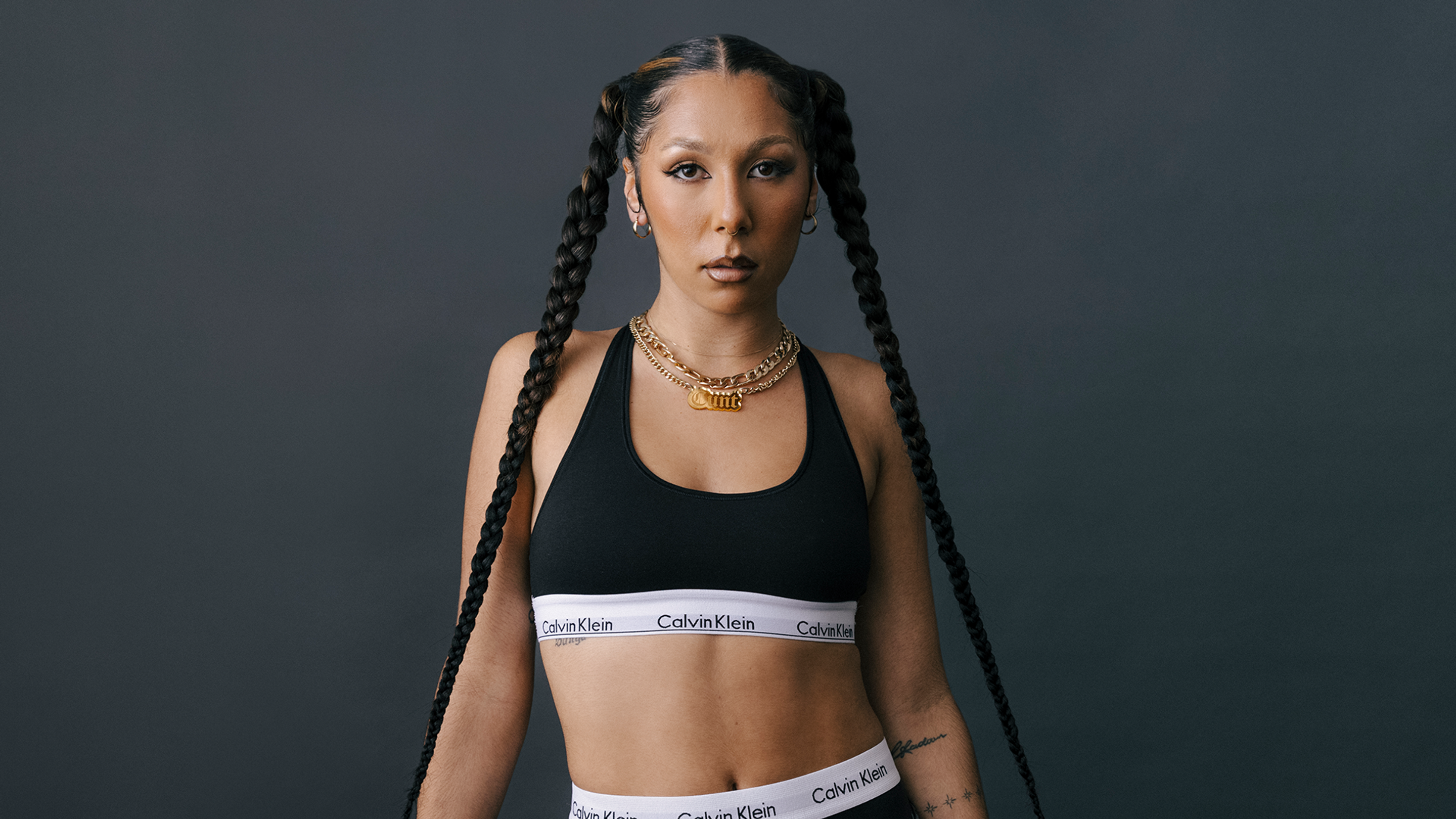 Miss Kaninna poses in a croptop, each hand pulling down her long braids