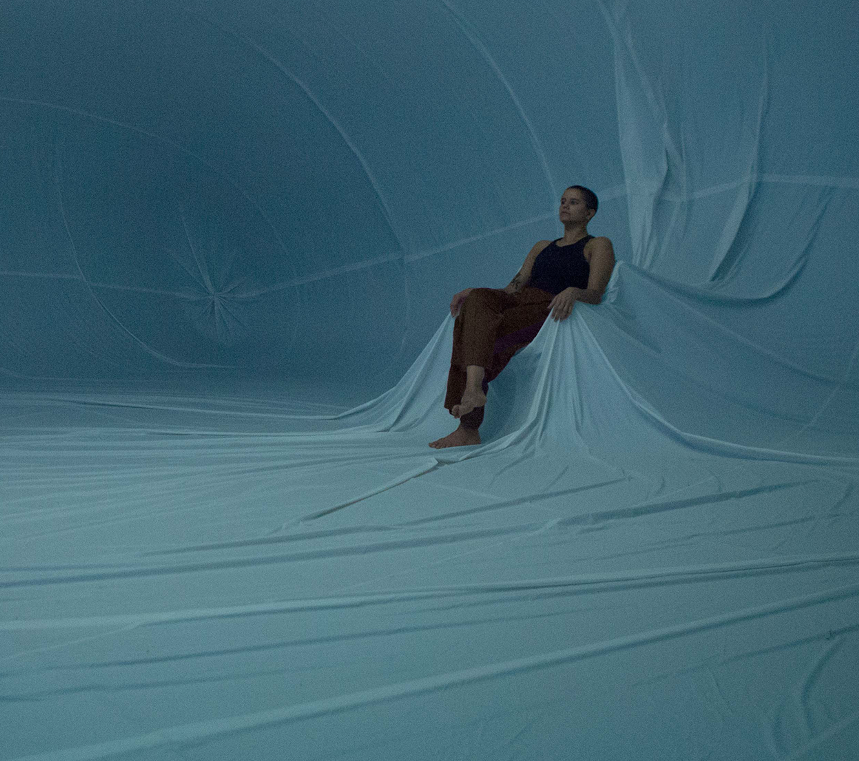A performer is pictured sitting within a vast inflatable space.