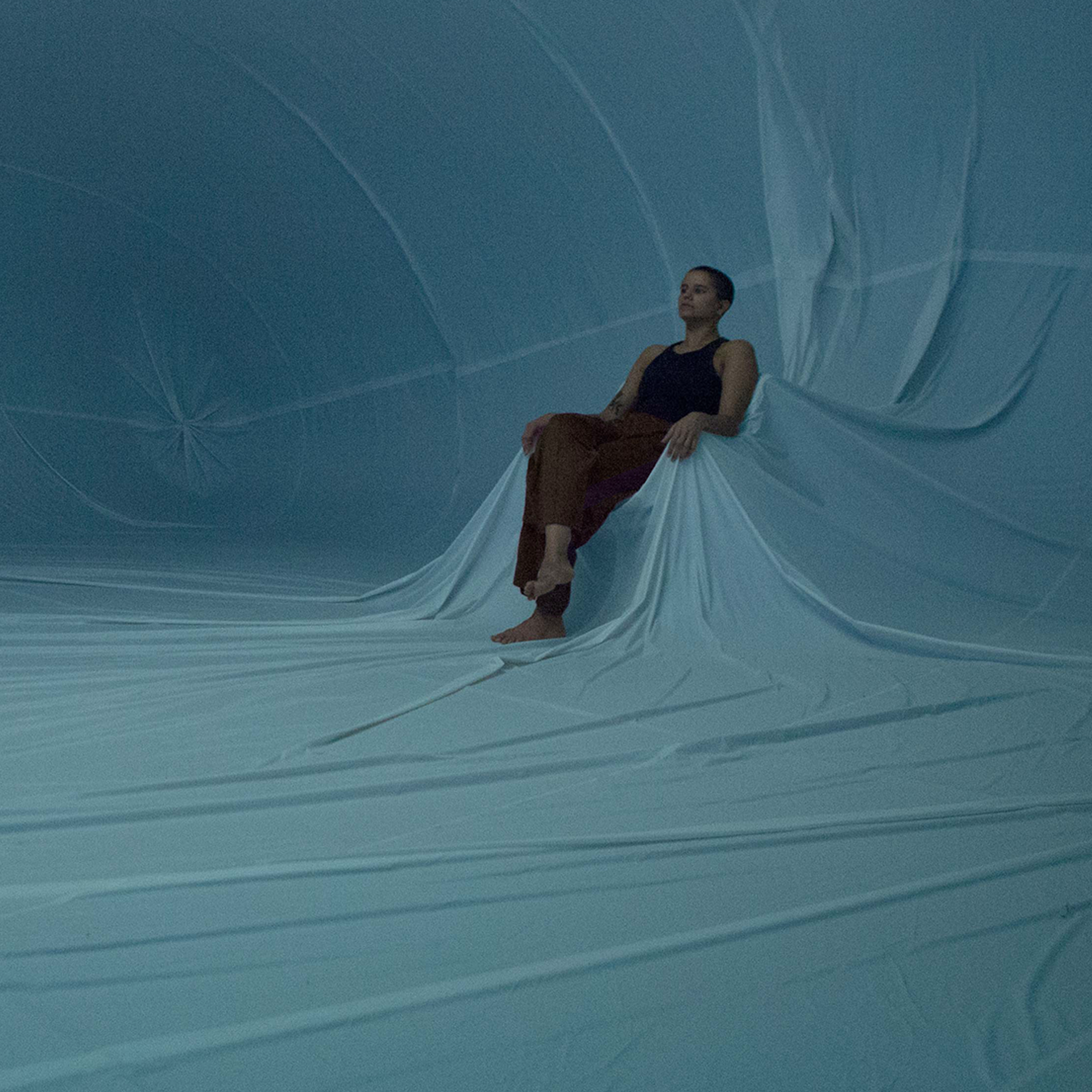 A performer is pictured sitting within a vast inflatable space.