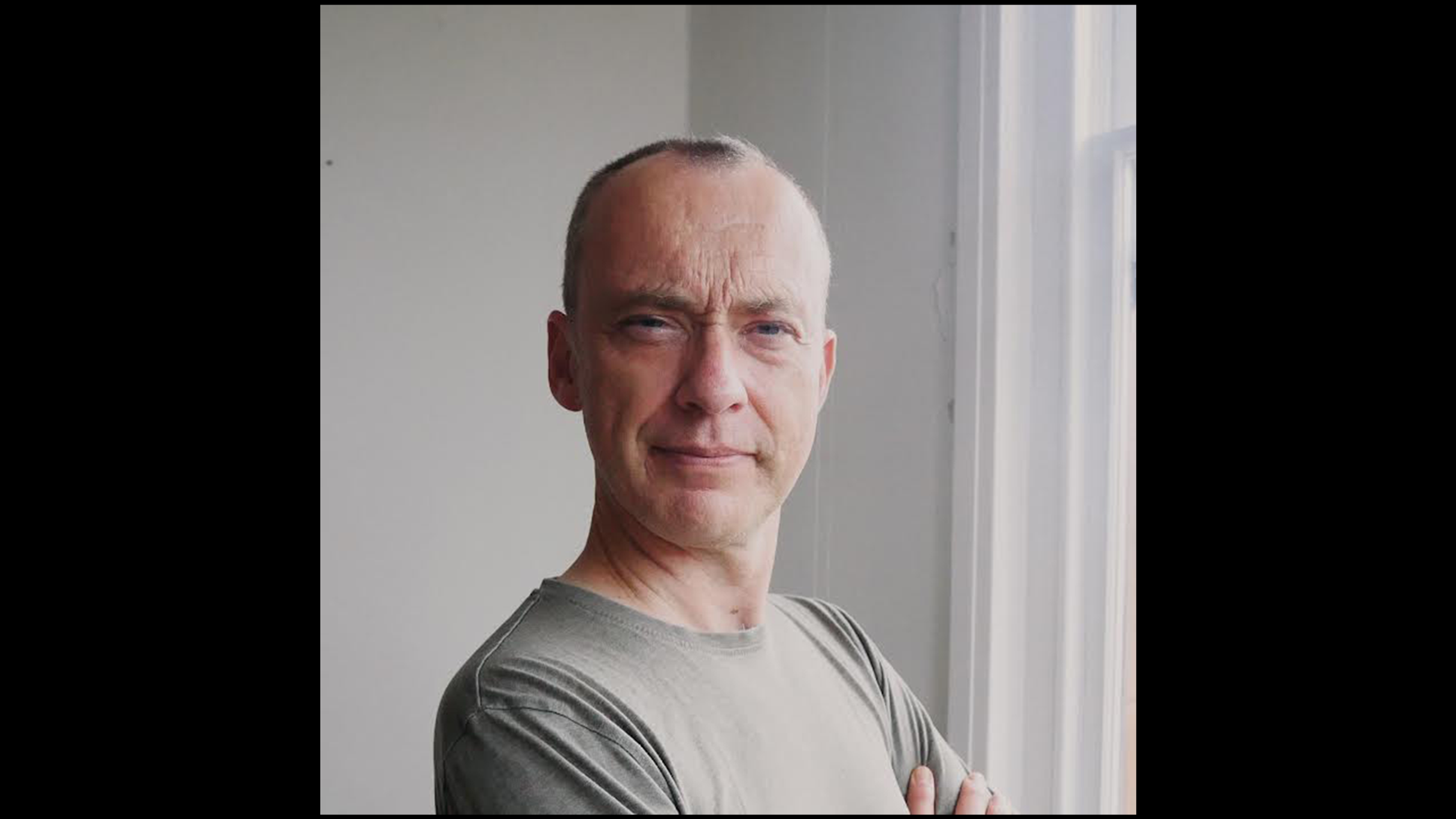 A close up of Richard Youngs posing in front of a bright window. His face turned to face the camera 