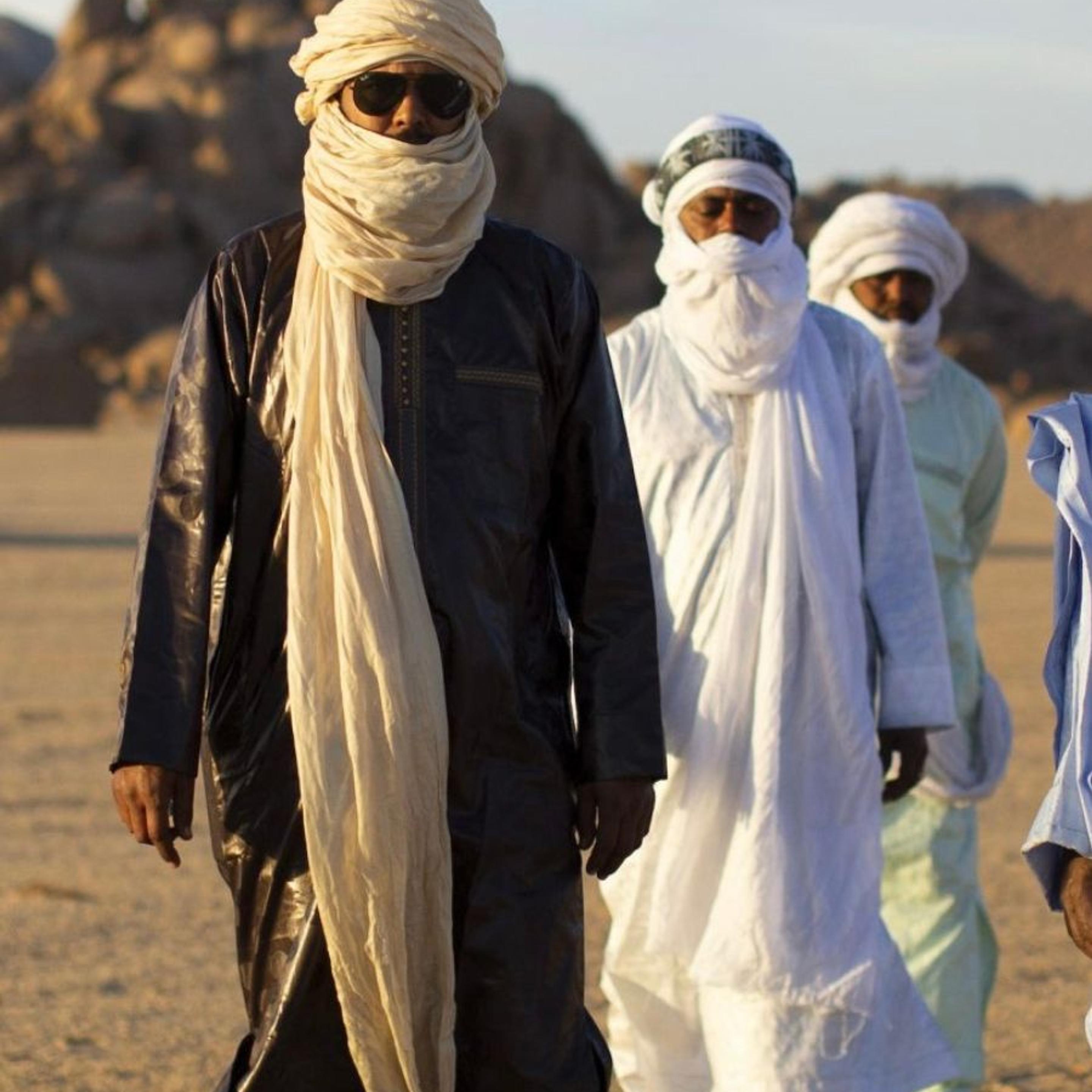 A group of men wearing white and blue robes and head coverings, in the desert.