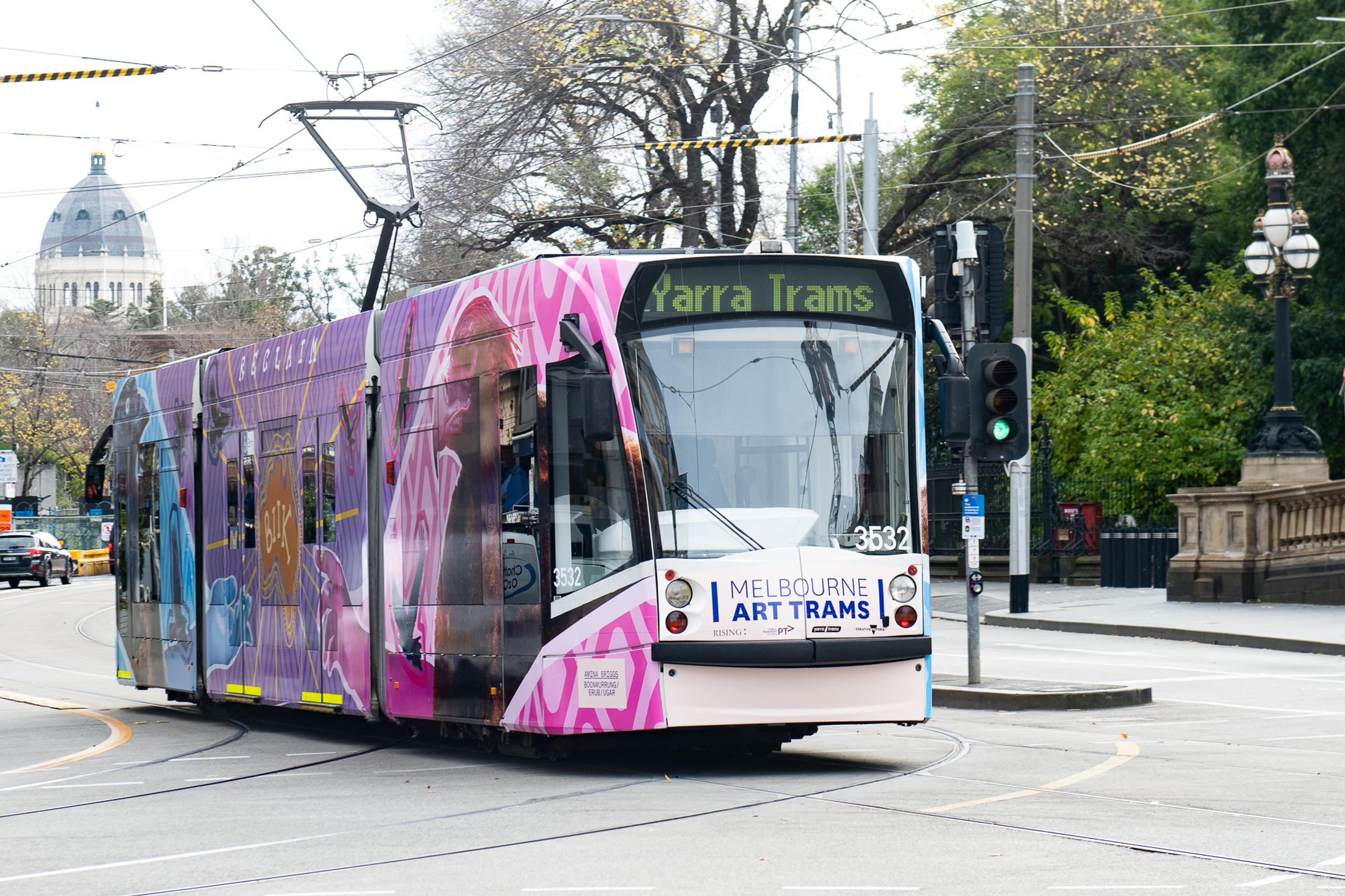 Amina Briggs' Art tram driving down Spring Street, alongside Parliament House Melbourne, with city buildings in the backdrop.