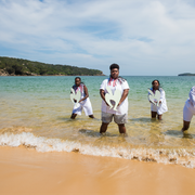 A group of people stand in the shallows of a tropical beach, holding cut-out shapes. 