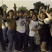 A grainy still from 1986 documentary, Heavy Metal Parking Lot, featuring '80s heavy metal fans yelling 'Judas Priest'