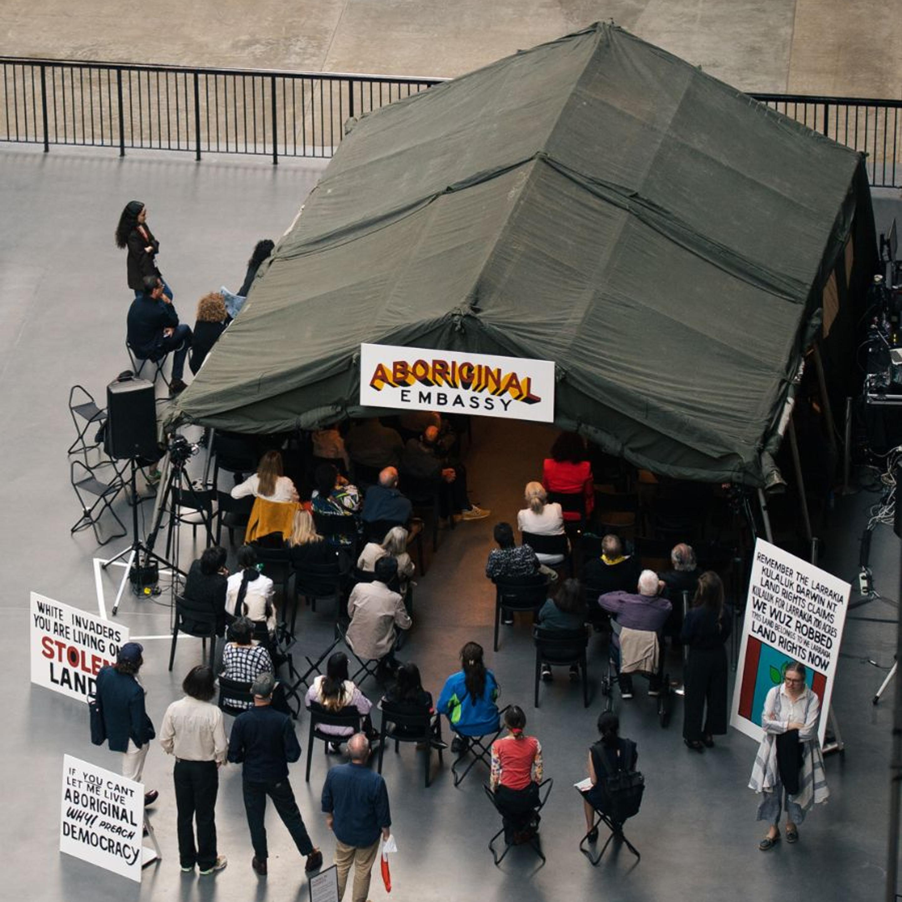 A tent sits within a large gallery space, teeming with visitors. A sign above the tent reads: "Aboriginal Embassy"