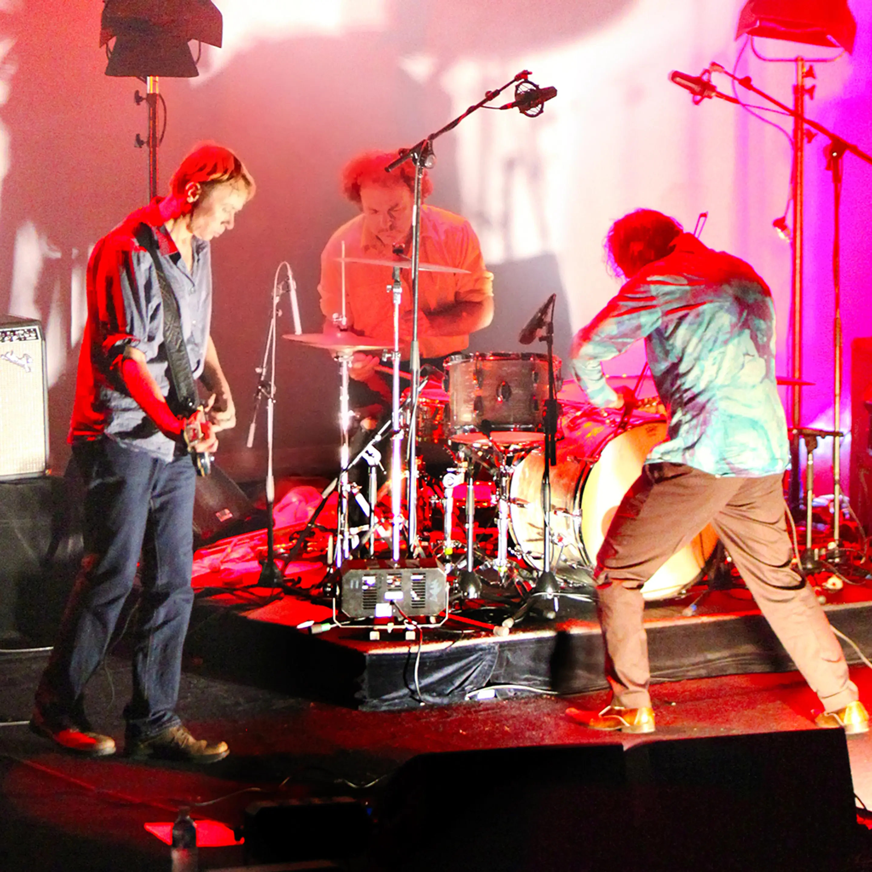 Three members of Dirty Three face each other on a stage, jamming together.