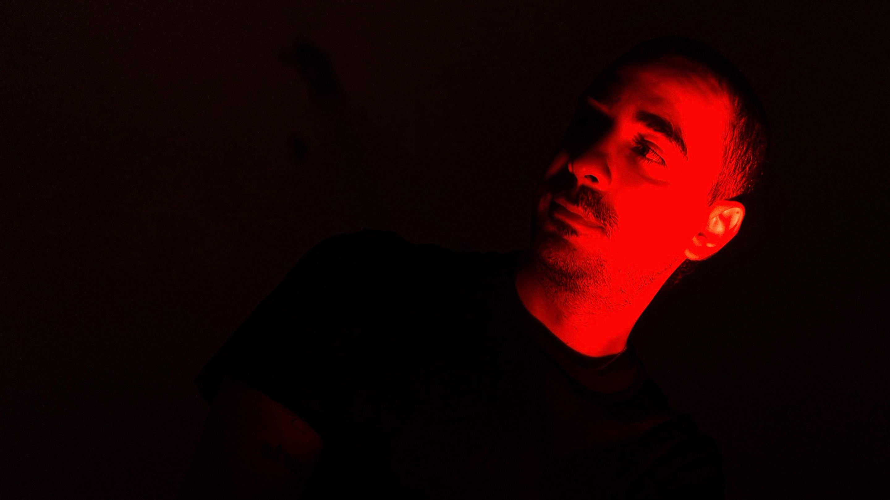Moktar looking off side of screen at night, bathed in red light on one half of his face and body