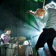 A dynamic live music scene with a violinist in motion, a drummer, and a bassist performing on stage under bright lights, capturing a moment of artistic expression.
