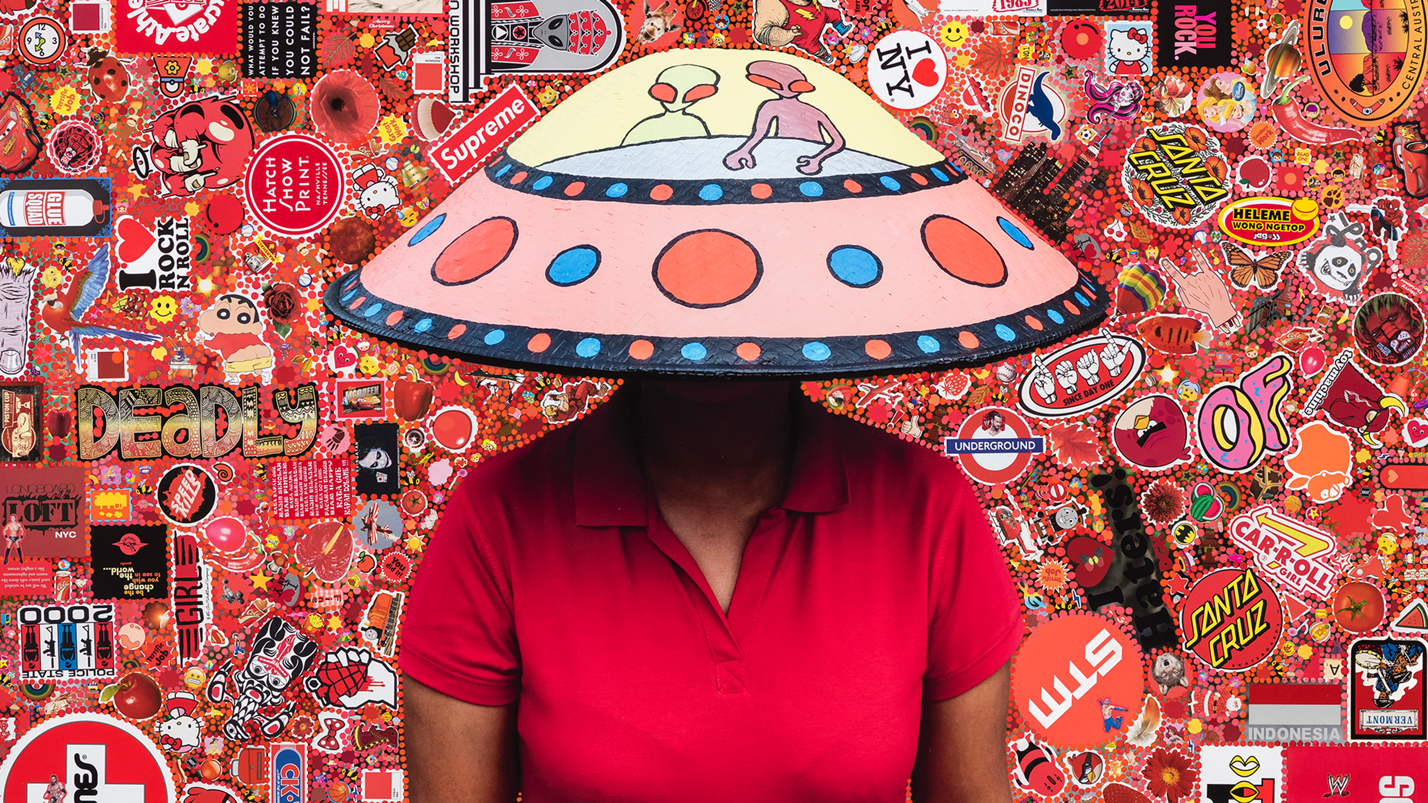A person wears a conical hat painted like a UFO with aliens. The background is a mish mash of similarly coloured pop culture references.
