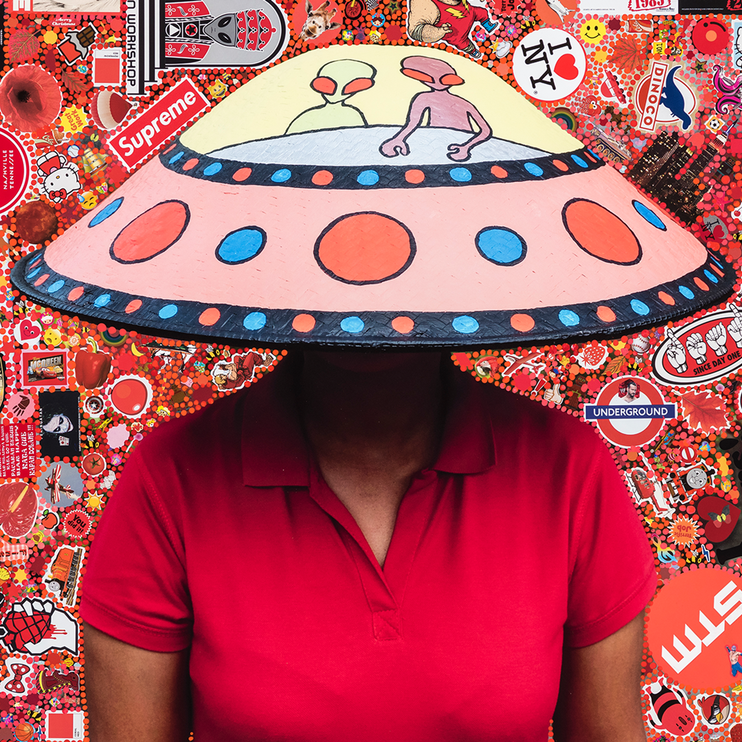 A person wears a conical hat painted like a UFO with aliens. The background is a mish mash of similarly coloured pop culture references.